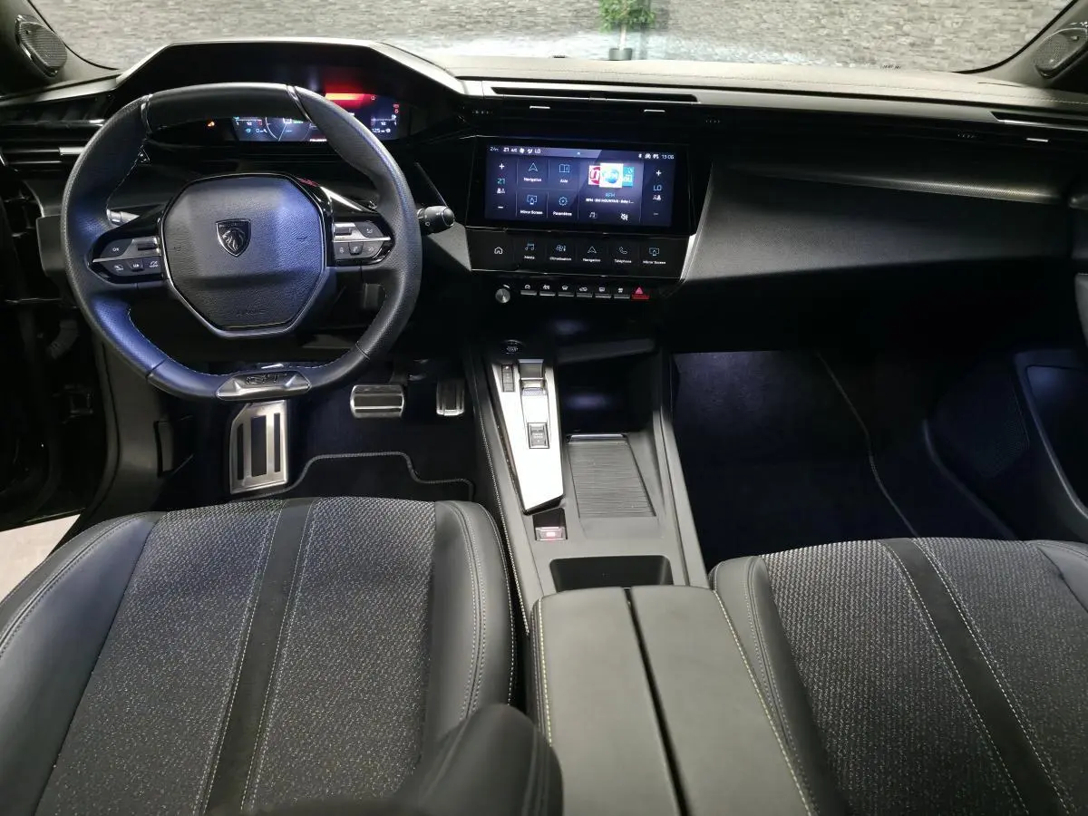 Vue intérieure avant de la Peugeot 308 SW GT 2024 noire, avec volant cuir, écran tactile central et sièges tissu/TEP.