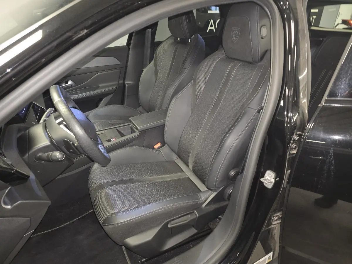 Vue intérieure côté conducteur de la Peugeot 308 SW 2024 noire, sièges tissu/TEP avec logo Peugeot brodé sur appuie-tête.