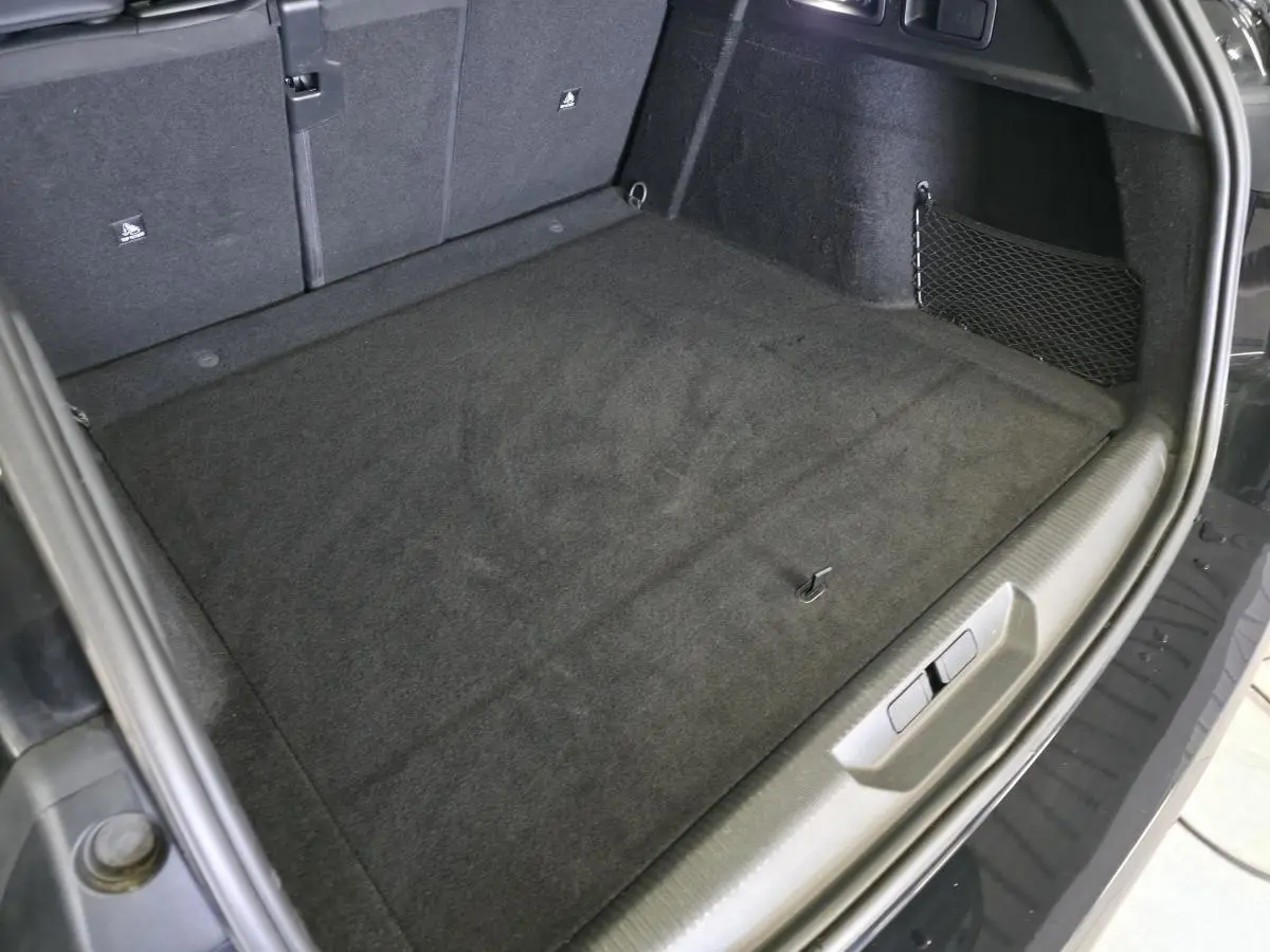 Vue intérieure du coffre arrière noir du Peugeot 308 SW 1.6 PHEV 2024, avec tapis et filet de rangement latéral.