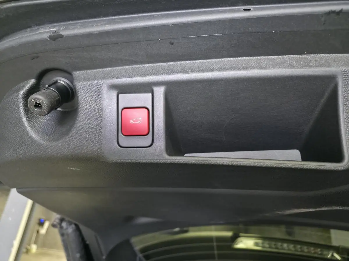 Gros plan sur le bouton rouge d'ouverture motorisée du hayon du coffre du Peugeot 308 SW noir, intérieur du hayon visible.