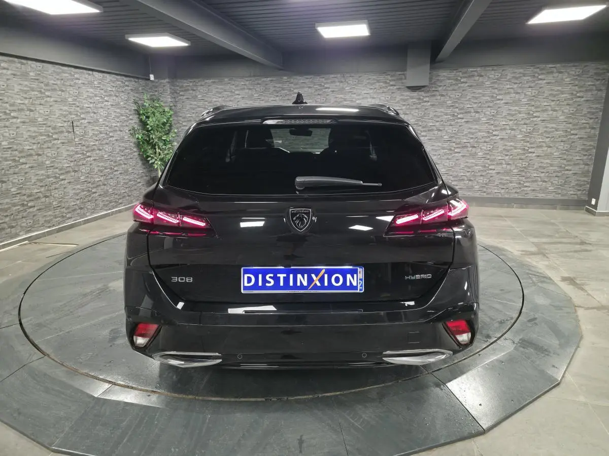Vue arrière d'une Peugeot 308 SW hybride noire avec feux arrière LED allumés dans un showroom.