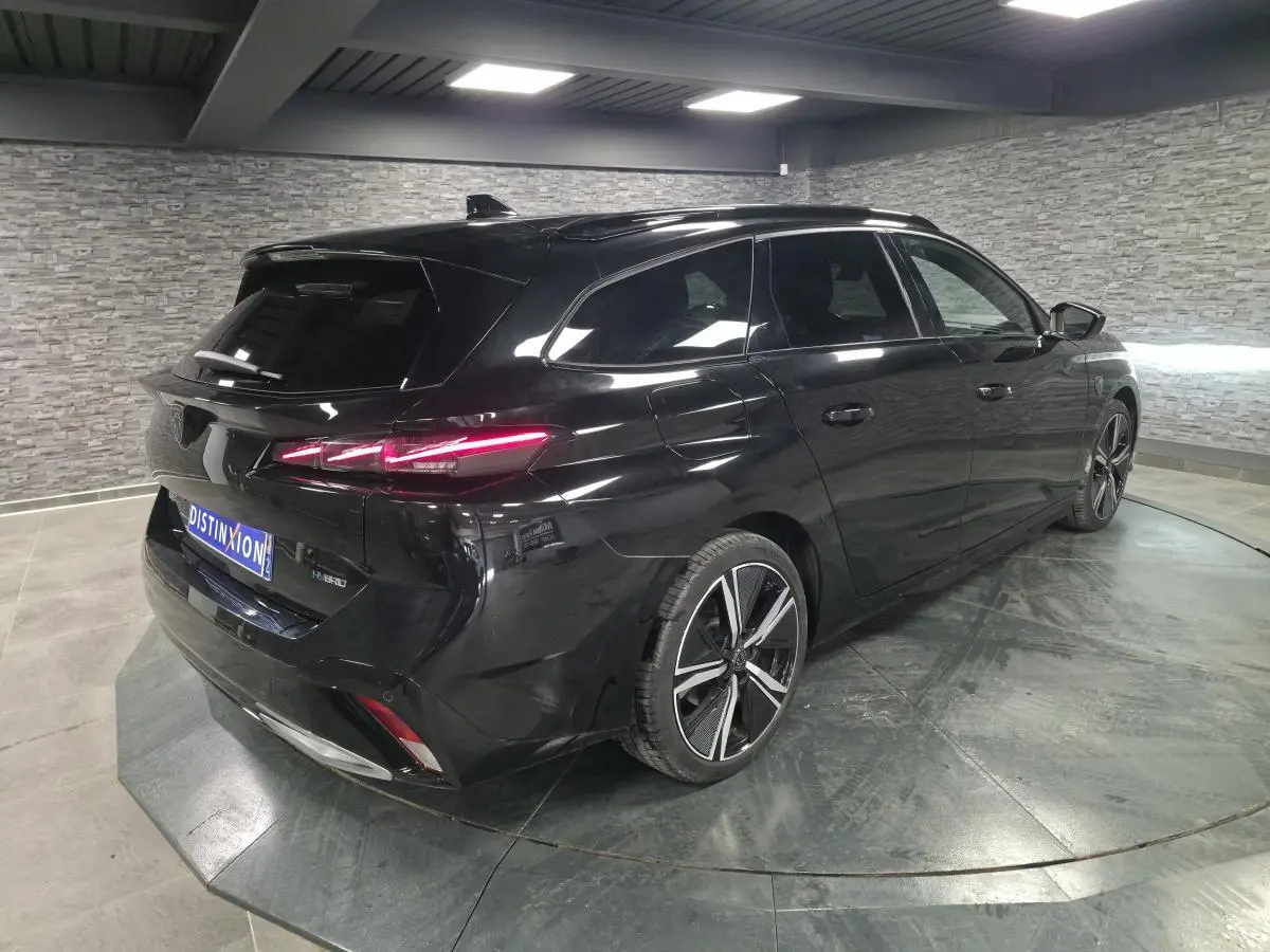 Peugeot 308 SW hybride noire vue en 3/4 arrière droit, feux arrière LED allumés et jantes alliage 18 pouces.