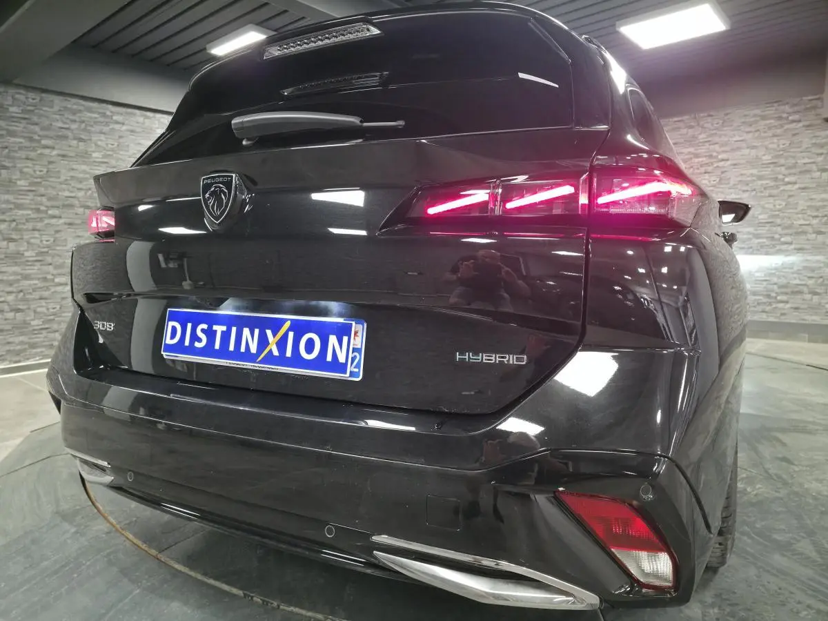 Vue 3/4 arrière d'une Peugeot 308 SW hybride noire avec feux arrière LED allumés et logo lion chromé.