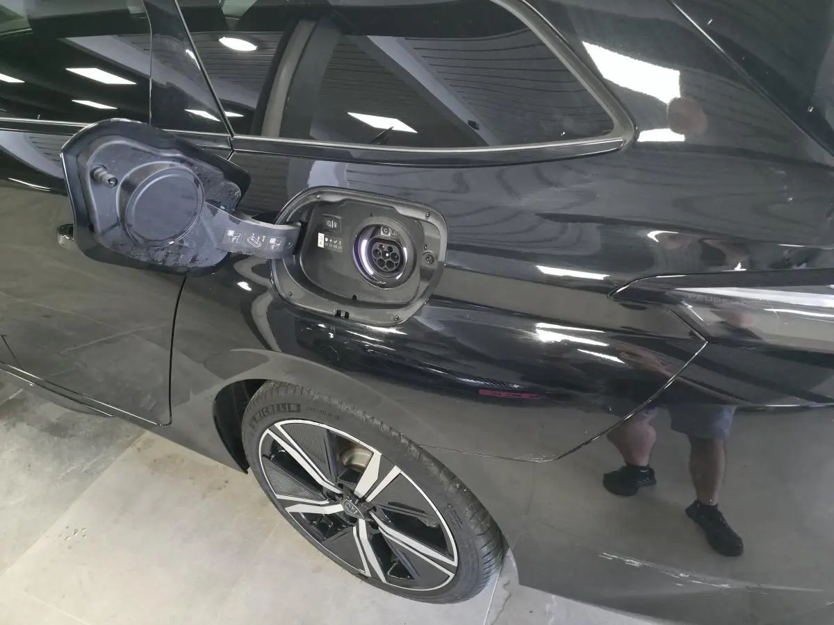 Prise de recharge ouverte côté arrière gauche d’une Peugeot 308 SW noire avec jante alliage 18 pouces.