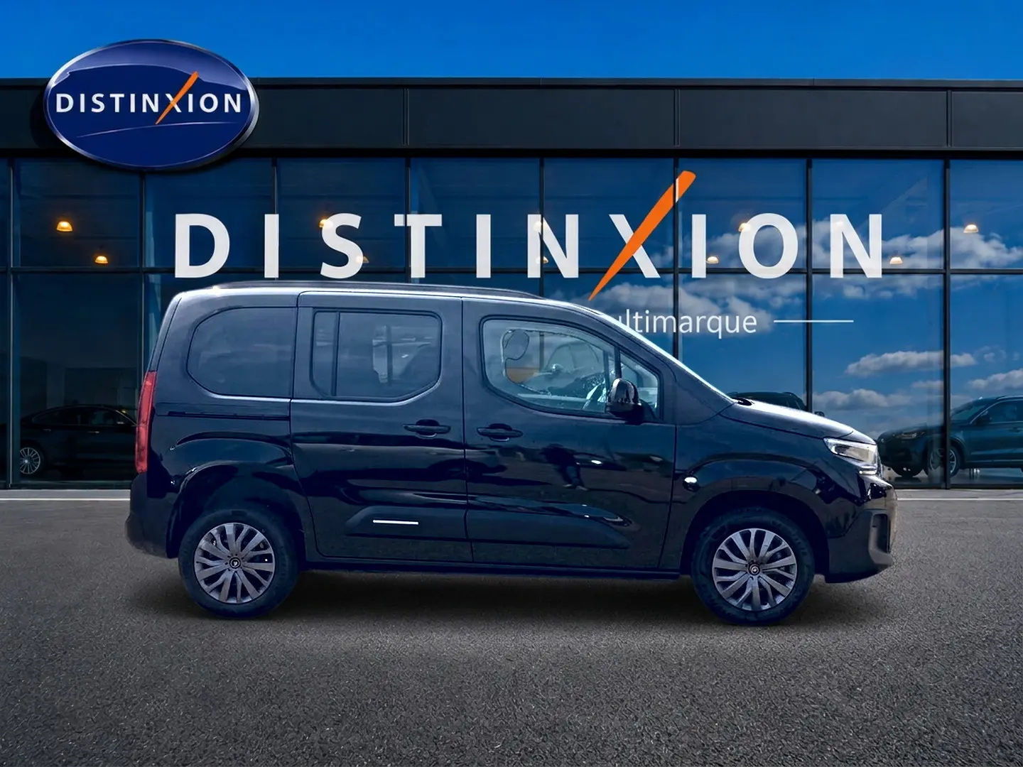 Profil droit du Citroën Berlingo noir 2026, avec barres de toit et jantes alliage visibles devant une vitrine Distinxion.