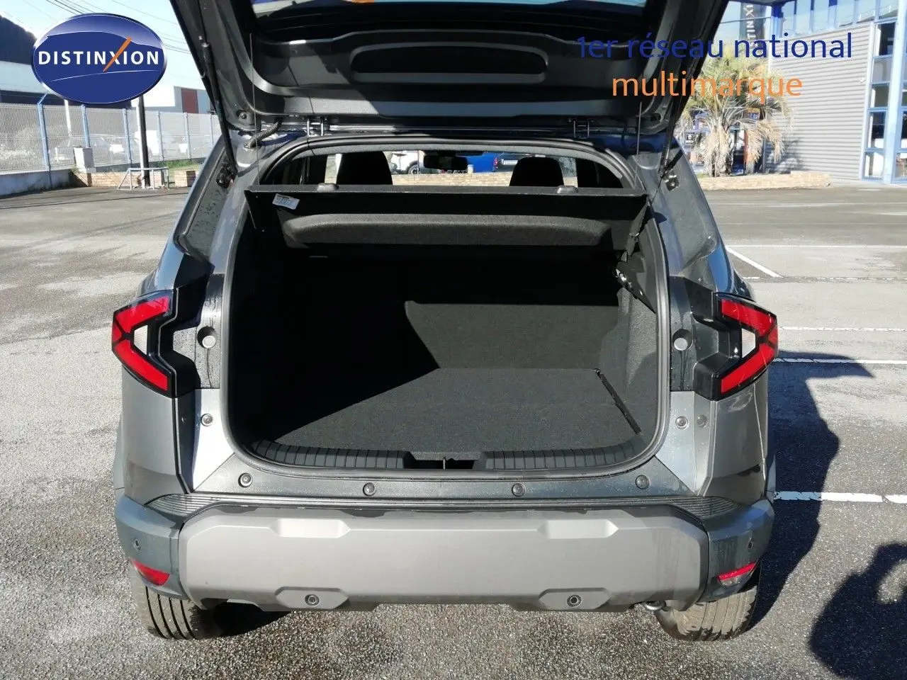 Vue arrière d'un Dacia Duster gris schiste métal 2026 avec coffre ouvert montrant l'espace de chargement vide.