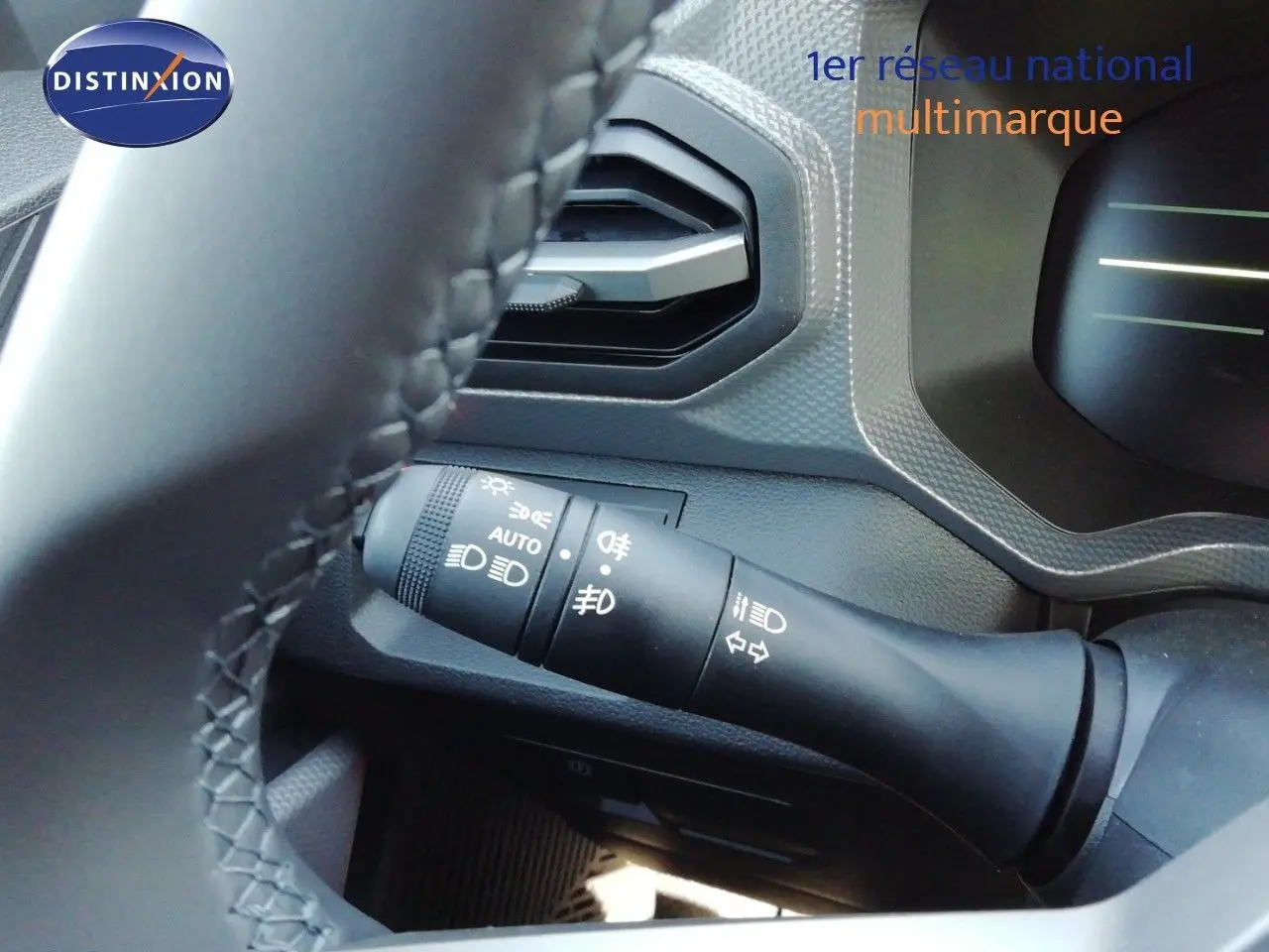 Gros plan sur la commande des feux à gauche du volant d’un Dacia Duster gris schiste métal, intérieur noir.