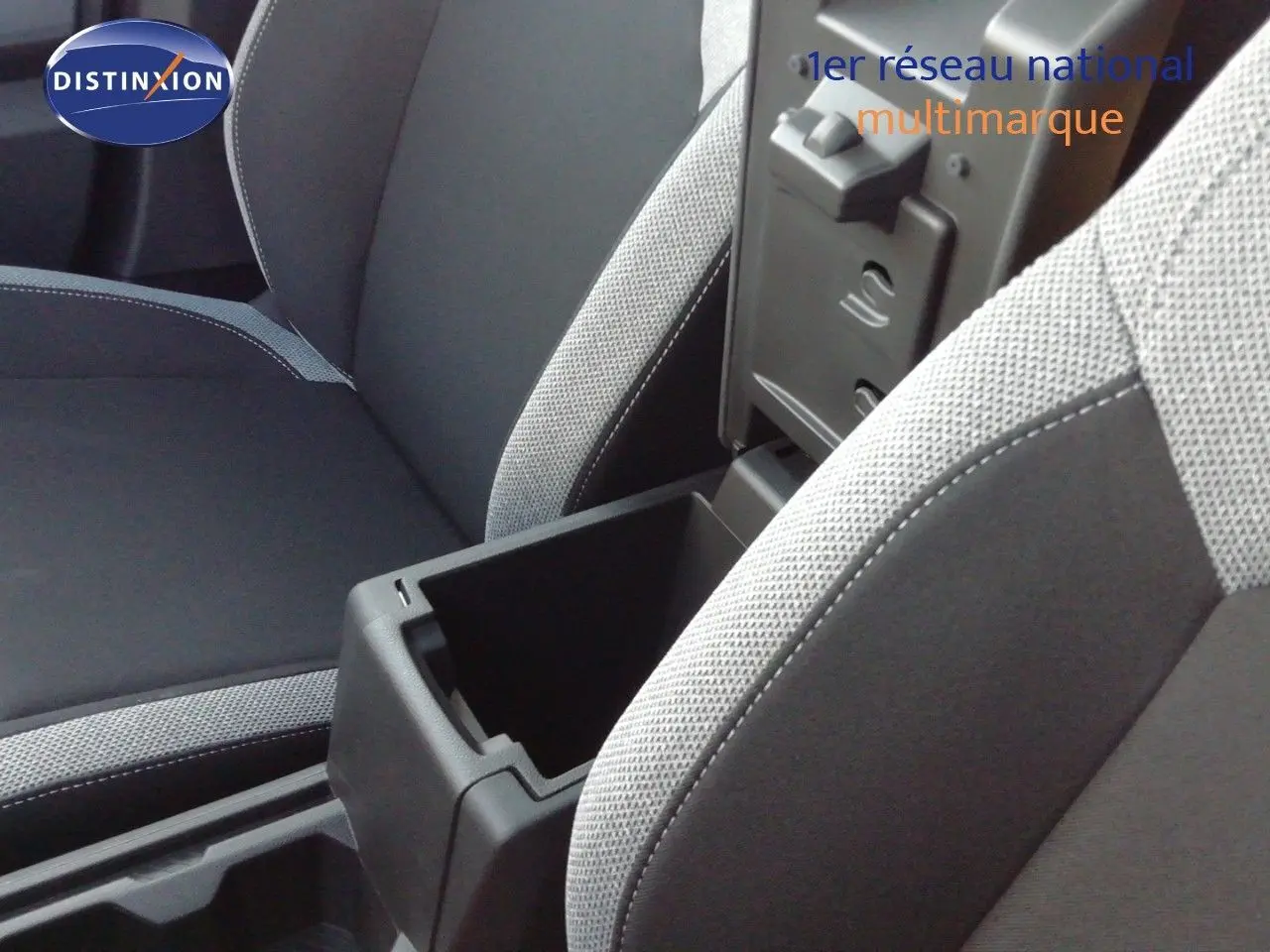 Vue rapprochée de l’intérieur du Dacia Duster 2026, montrant l’accoudoir central ouvert et les sièges tissu gris clair et noir.