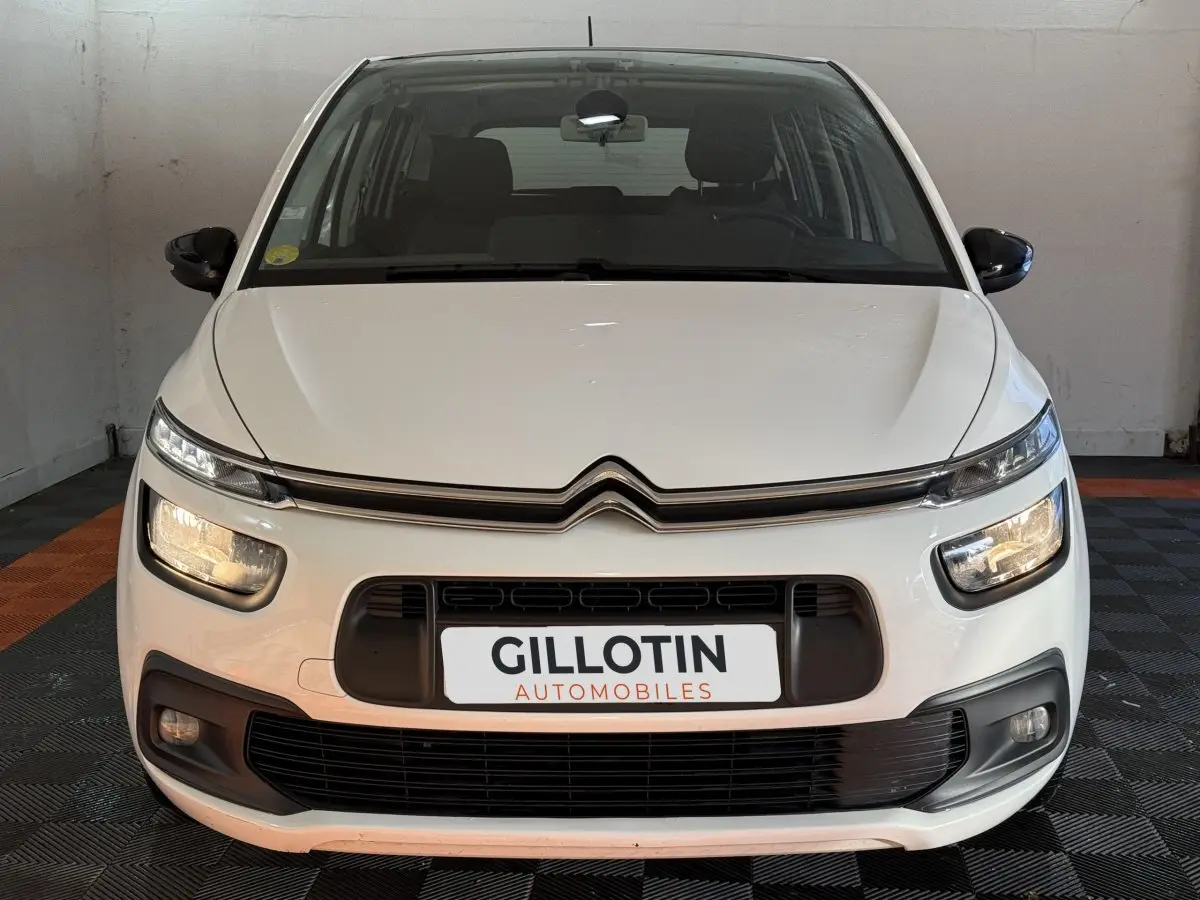 Vue frontale d'un Citroën Grand C4 Spacetourer blanc avec phares allumés dans un garage.