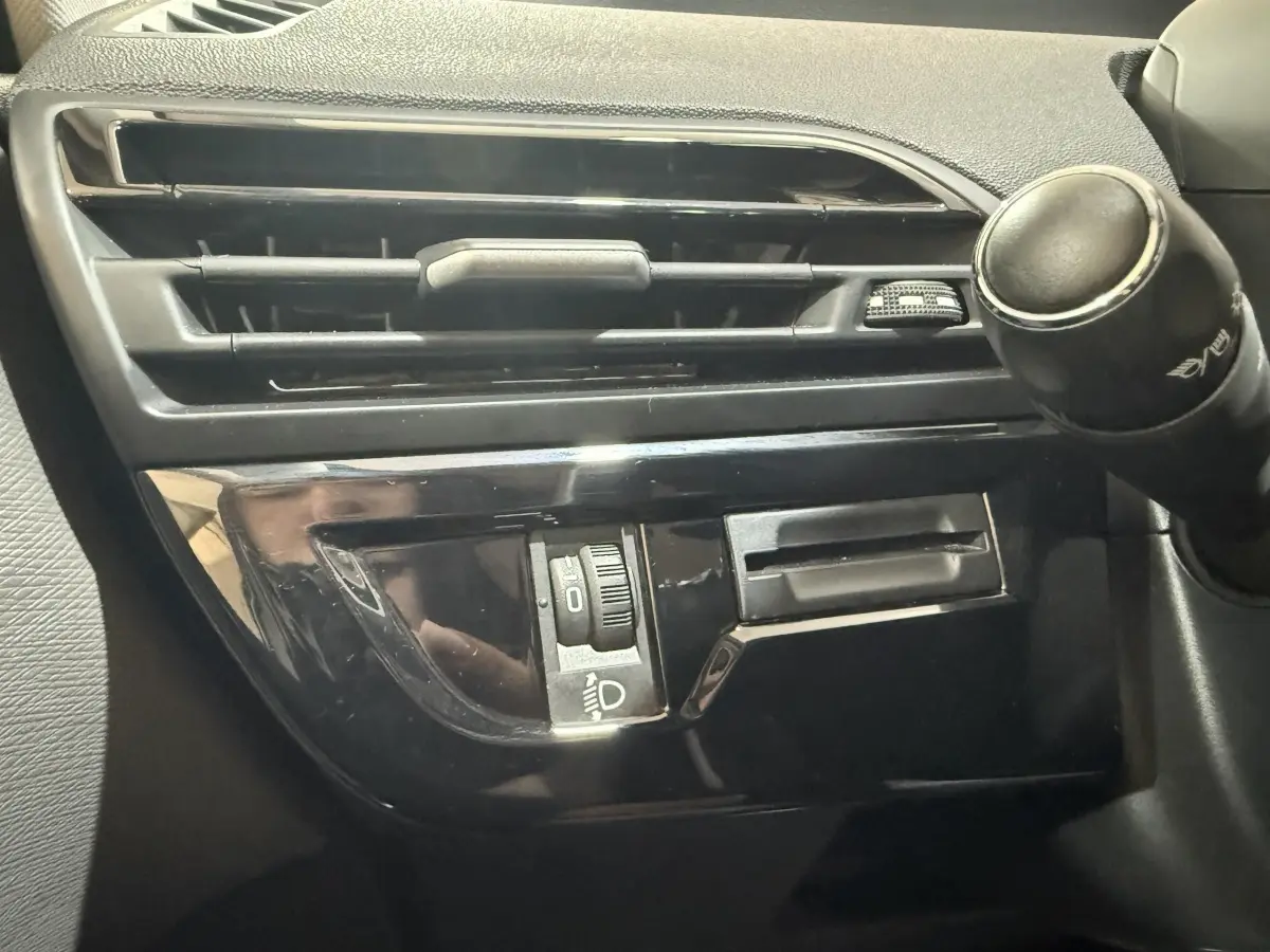 Détail intérieur côté gauche du tableau de bord noir brillant avec commande des phares et sortie d'air du Citroën Grand C4 Spacetourer.