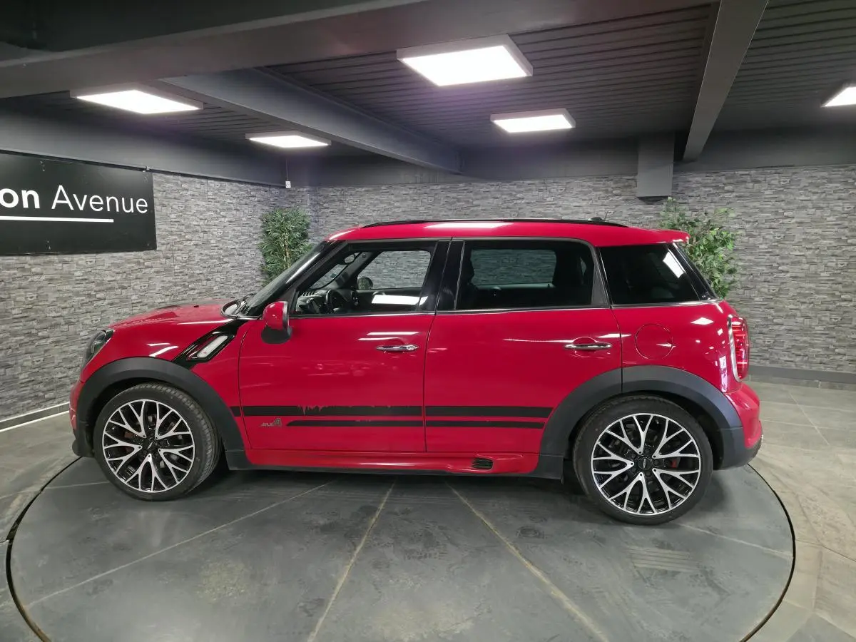 Profil droit d'une MINI Countryman John Cooper Works rouge avec bandes sport noires et jantes alliage distinctives.