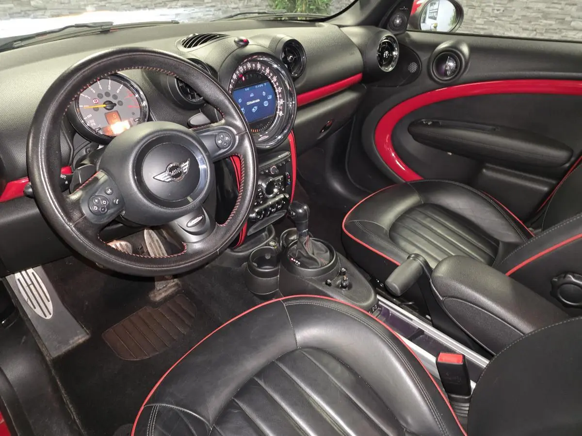 Vue intérieure côté conducteur de la MINI Countryman John Cooper Works 2015, cuir noir avec surpiqûres rouges et inserts rouges sur tableau de bord.