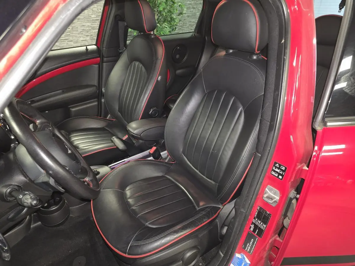 Vue intérieure côté conducteur d'une MINI Countryman John Cooper Works 2015 rouge, sièges cuir noirs avec surpiqûres rouges.