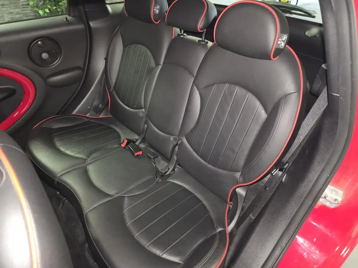 Vue intérieure côté arrière droit de la MINI John Cooper Works, sièges cuir noirs avec surpiqûres rouges et détails rouges sur portière rouge.