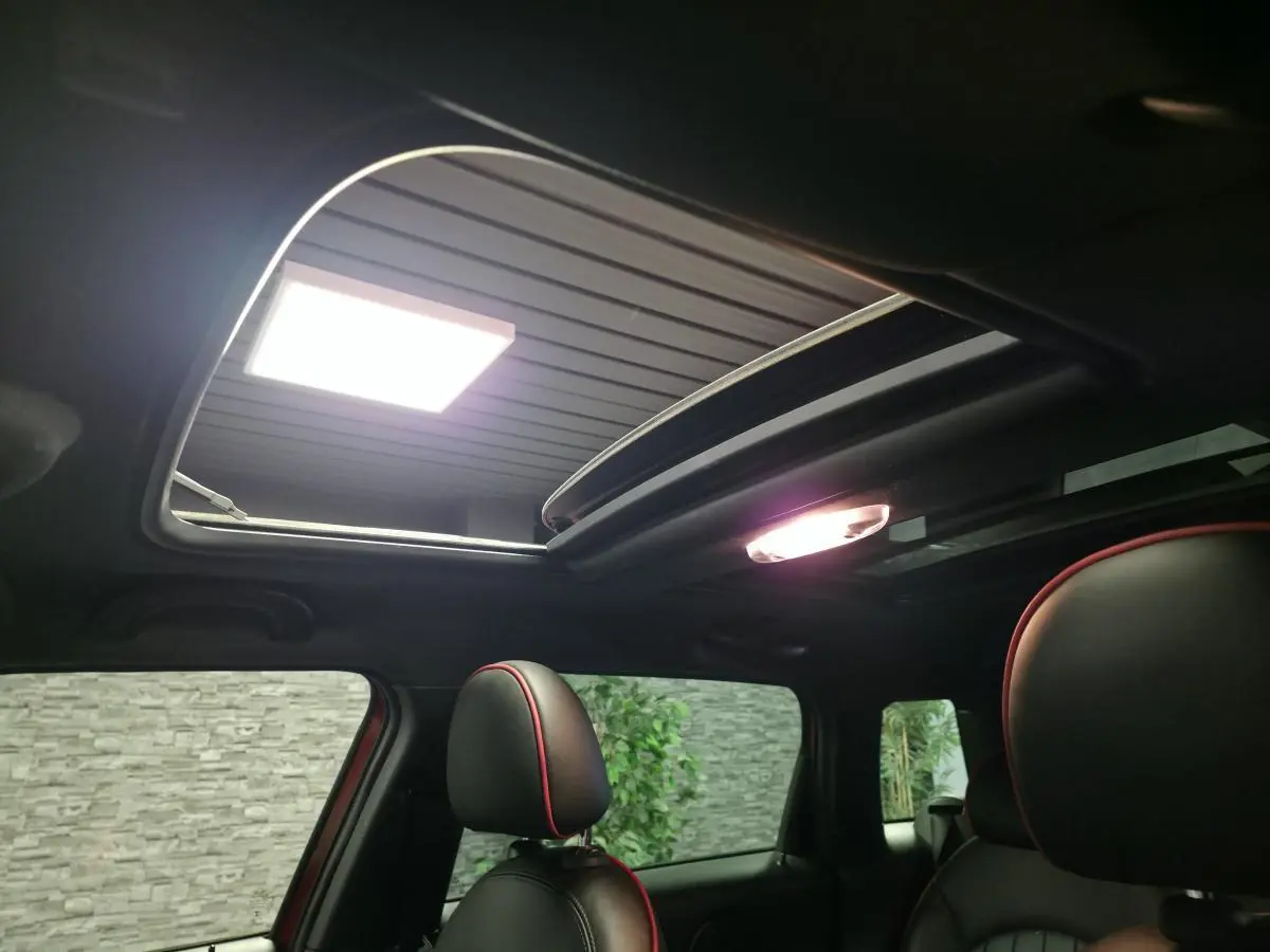 Vue intérieure du toit ouvrant électrique et des sièges avant noirs avec surpiqûres rouges du MINI Countryman John Cooper Works rouge.