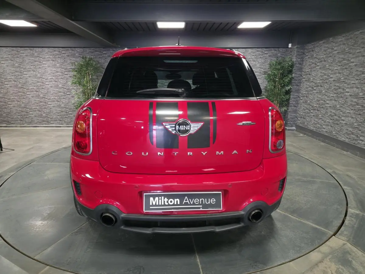 Vue arrière d'une MINI Countryman John Cooper Works rouge avec bandes noires sport et double sortie d'échappement.