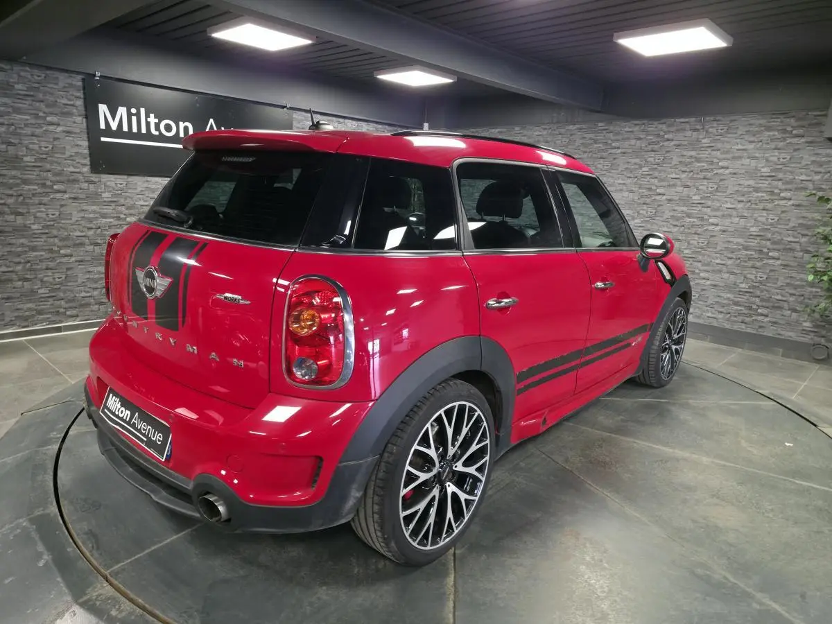 Vue 3/4 arrière droite d'une MINI Countryman John Cooper Works rouge avec bandes sport noires et jantes alliage.