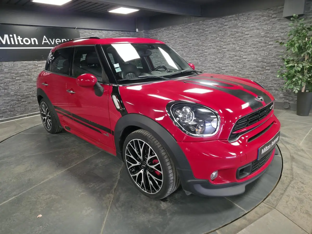 Vue 3/4 avant droite d'une MINI Countryman John Cooper Works rouge avec bandes noires sport et jantes noires à dessin complexe.