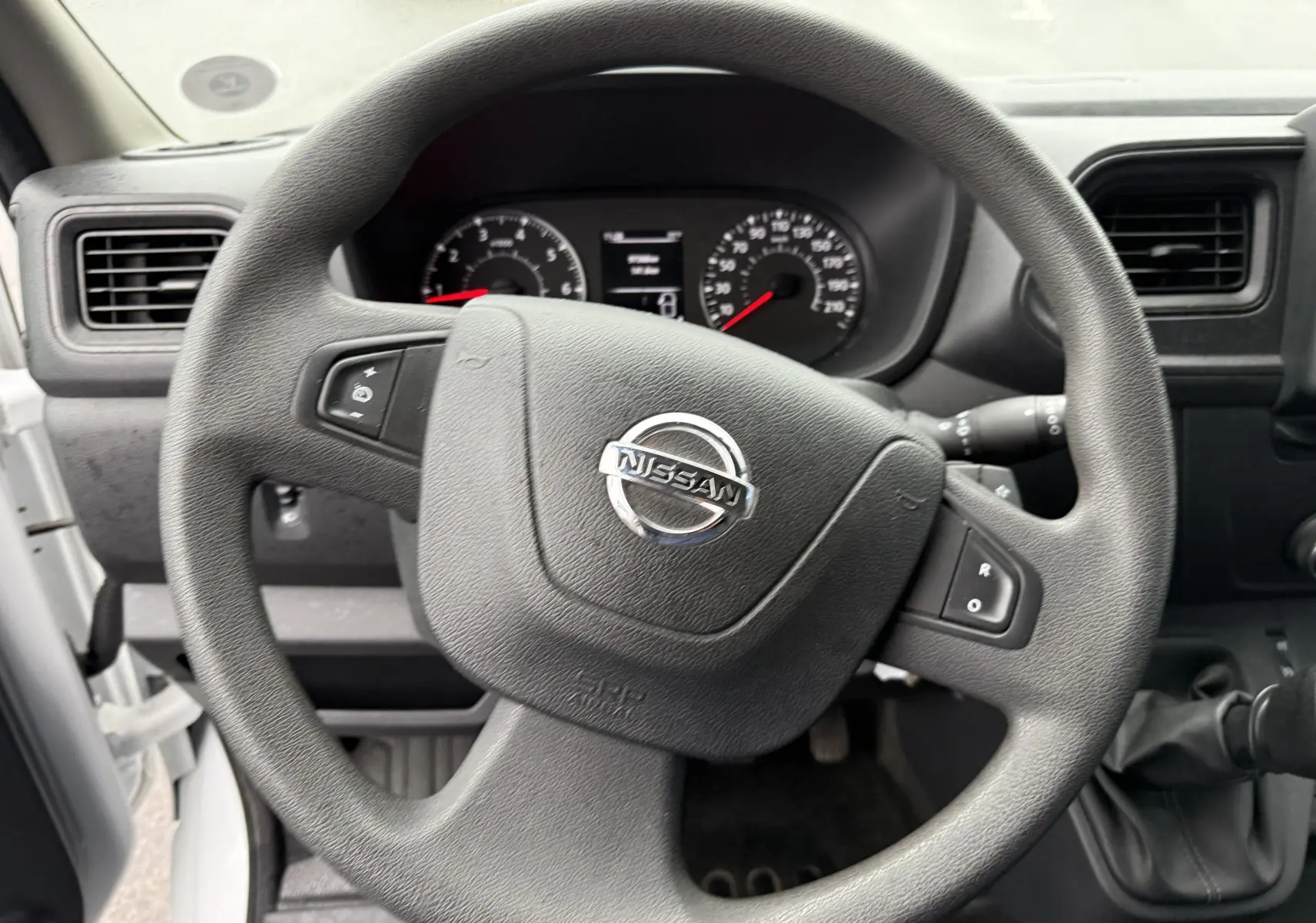 Vue rapprochée du volant noir du Nissan NV400 Fourgon 2020 avec tableau de bord et levier de vitesse manuel visibles.
