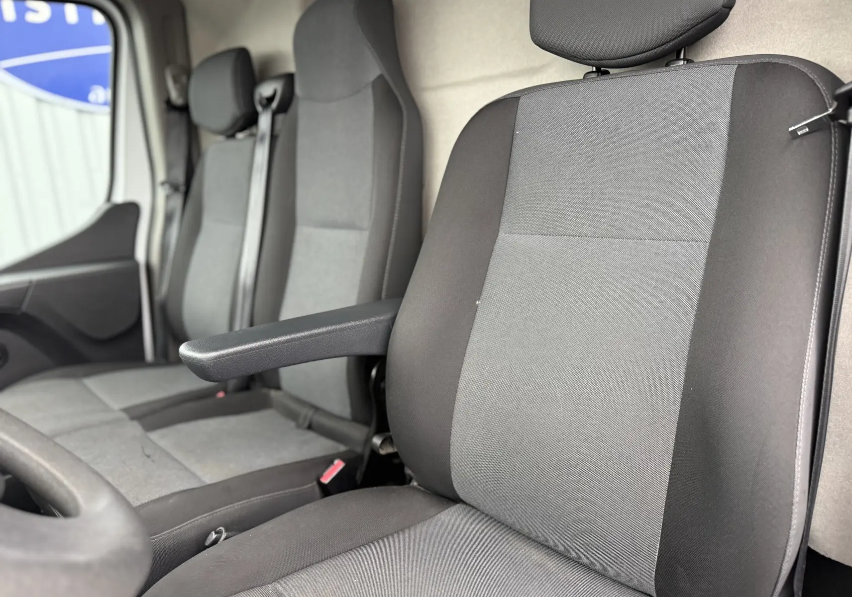 Gros plan sur les sièges avant gris et noirs du Nissan NV400 Fourgon blanc, version 2020, avec accoudoir côté conducteur.