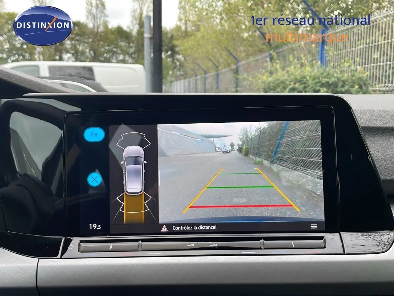 Vue de l'écran multimédia affichant la caméra de recul d'une Volkswagen Golf VIII bleu lapiz metal en stationnement.