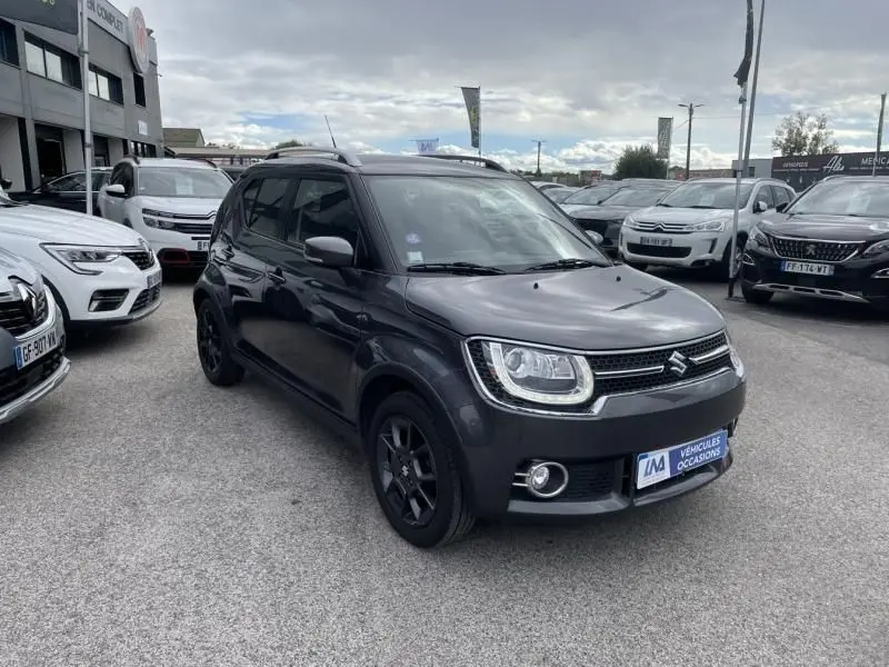 Suzuki Ignis 1.2 Dualjet Hybrid gris foncé métal vue 3/4 avant avec jantes noires sur parking extérieur.