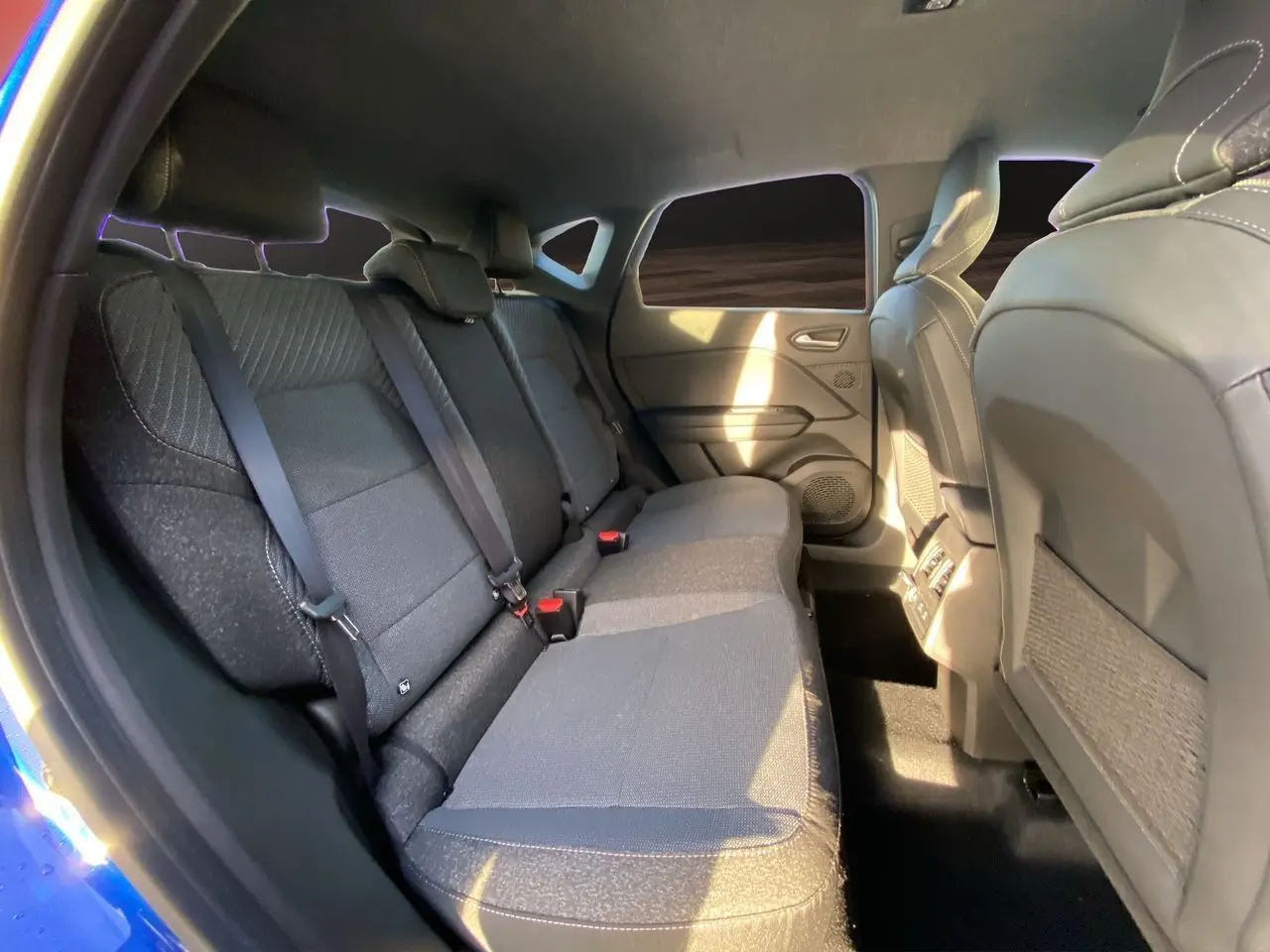 Vue intérieure arrière côté gauche du Renault Captur 2025 bleu Iron avec sièges tissu et toit noir visible.