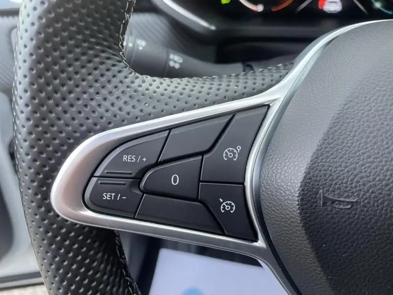 Gros plan sur les commandes de régulateur de vitesse au volant en cuir perforé du Renault Captur blanc nacré 2023.