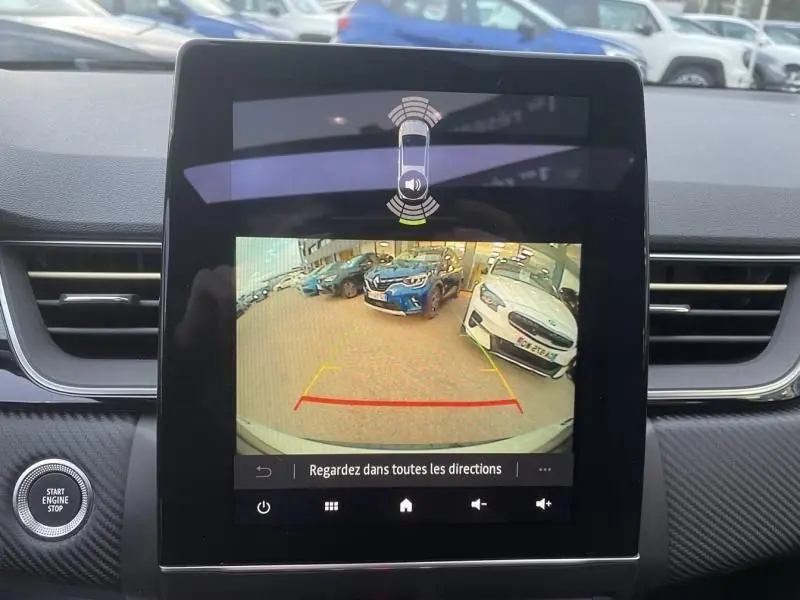 Vue de l'écran central montrant la caméra de recul d'un Renault Captur blanc nacré, avec l'affichage des aides au stationnement.