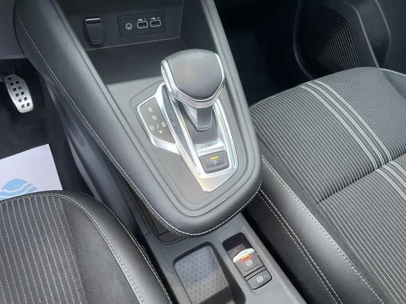 Gros plan sur la console centrale du Renault Captur 1.6 E-Tech hybride 2023, avec levier de vitesse automatique et sièges noirs.