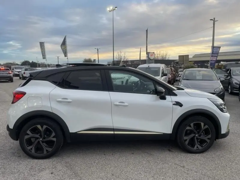 Vue de profil côté gauche d'un Renault Captur blanc nacré 2023 avec toit noir et jantes noires en concession.