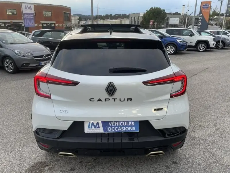 Vue arrière d'un Renault Captur blanc nacré 2023, version hybride 1.6 E-Tech 145 cv avec détails noirs et feux LED distinctifs.