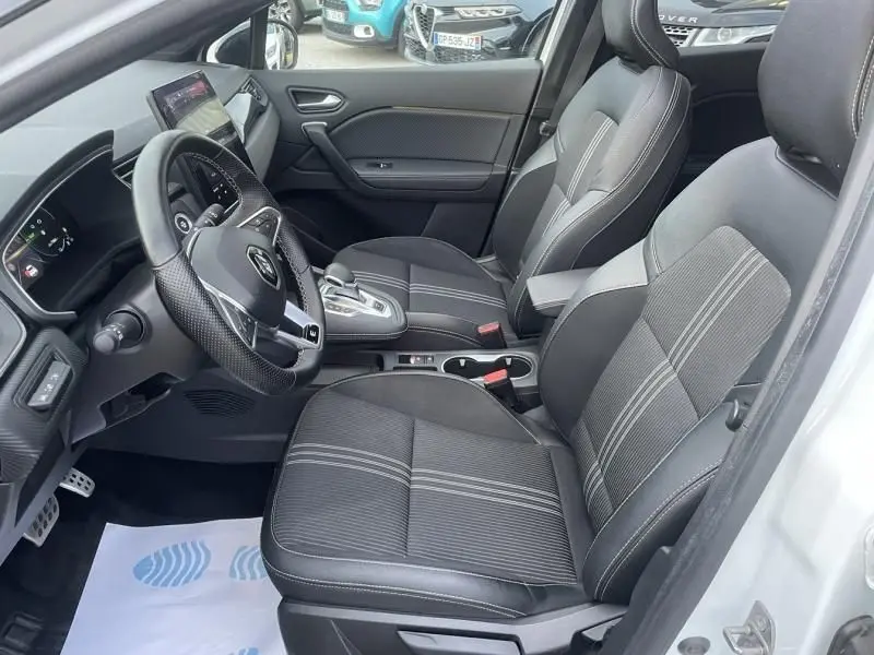 Vue intérieure côté gauche du Renault Captur 1.6 E-Tech hybride 2023, sièges noirs avec surpiqûres et volant multifonction.