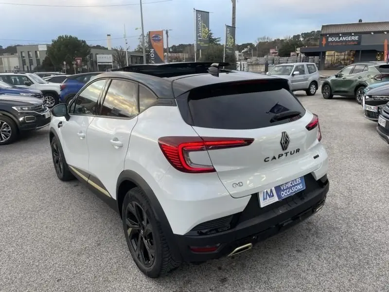 Vue 3/4 arrière droite d'un Renault Captur blanc nacré 2023, version hybride 1.6 E-Tech Engineered avec toit noir et jantes noires.