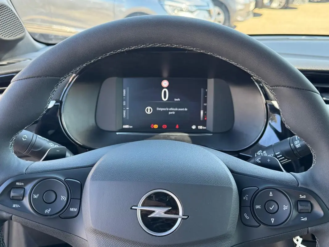 Vue rapprochée du volant noir de l’Opel Corsa rouge 2025 avec commandes intégrées et écran digital au tableau de bord.