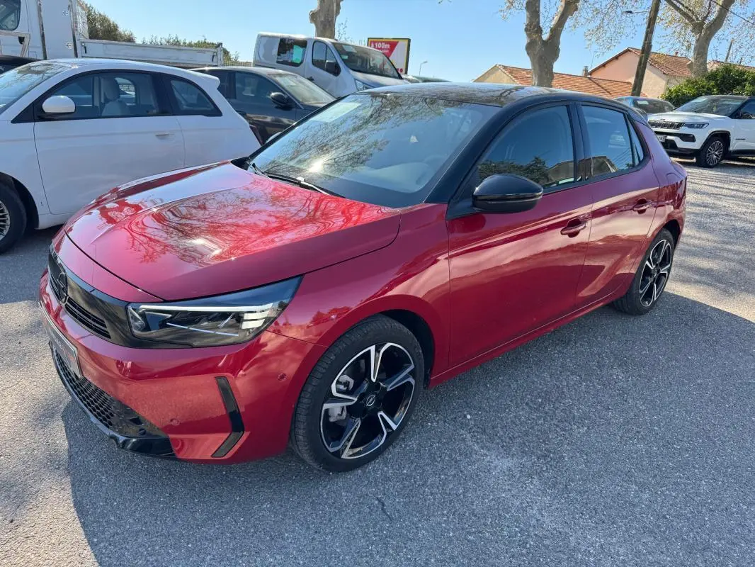 Opel Corsa rouge vue 3/4 avant droit, jantes alliage noires et toit noir brillant sous lumière naturelle.
