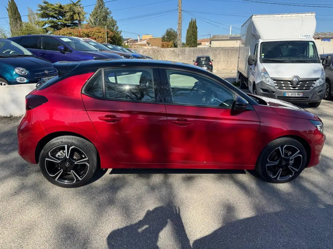 Vue latérale côté gauche d'une Opel Corsa rouge 2025 avec jantes alliage noires et toit noir.