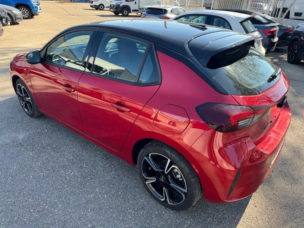 Vue 3/4 arrière droite d'une Opel Corsa rouge 2025 avec toit noir, jantes alliage 17 pouces et feux arrière fumés.