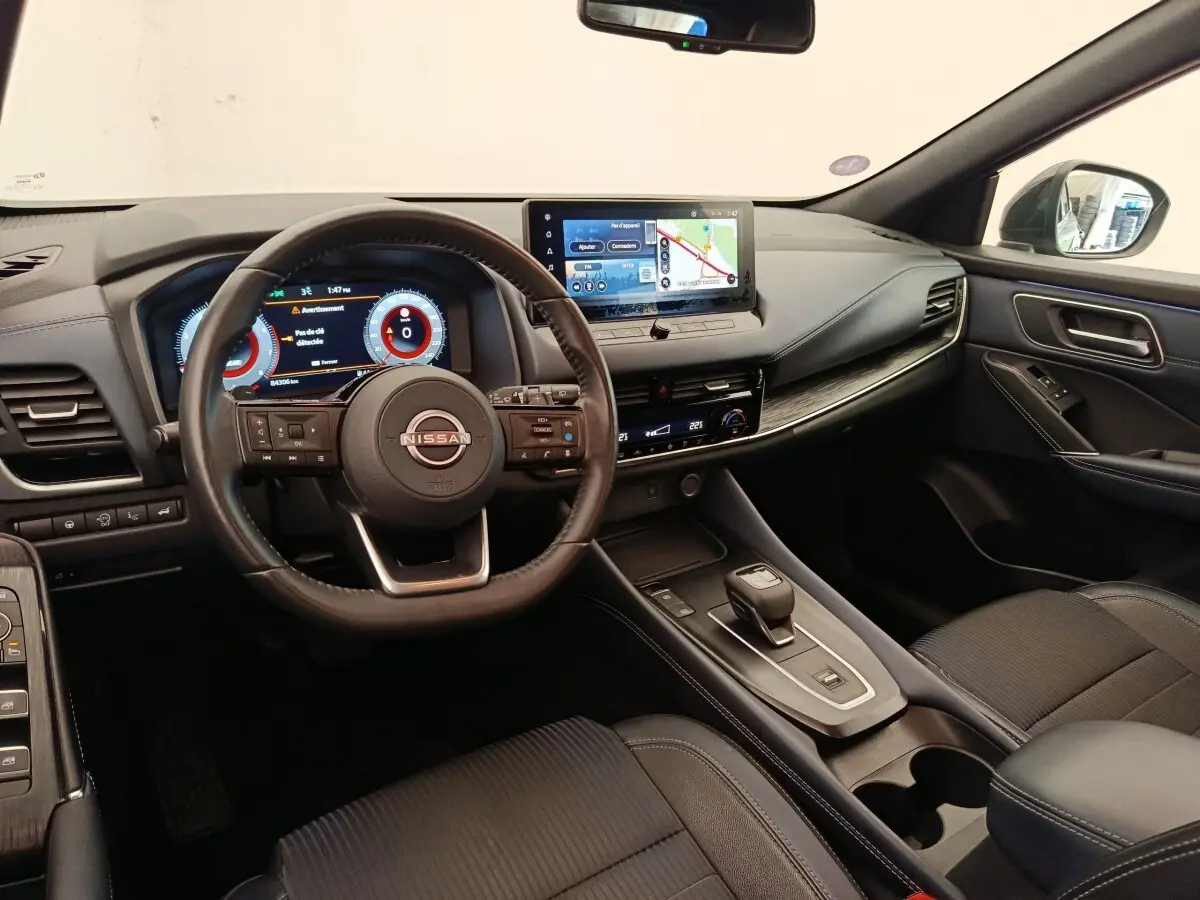 Intérieur noir du Nissan Qashqai 2023, vue du poste de conduite avec volant cuir et écran tactile central.