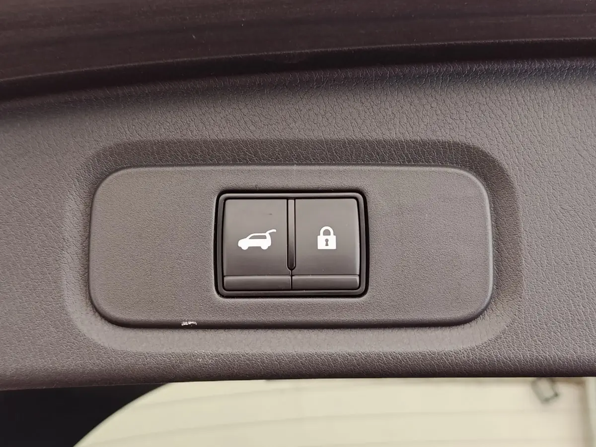 Boutons d'ouverture du coffre et de verrouillage intégrés dans le panneau intérieur du coffre d'un Nissan Qashqai noir.