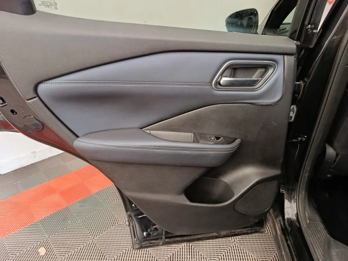 Vue intérieure de la porte arrière gauche noire du Nissan Qashqai 2023 avec accoudoir et commande de vitre.