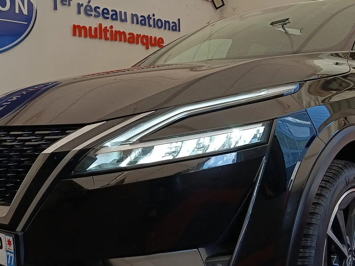 Gros plan sur l'avant droit noir du Nissan Qashqai 2023, mettant en valeur le phare LED fin et la calandre distinctive.