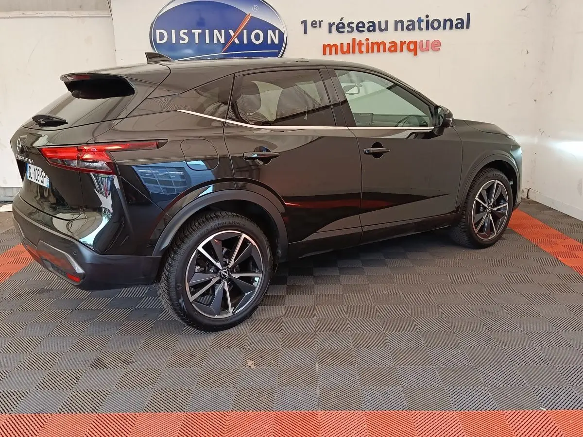 Vue 3/4 arrière droite du Nissan Qashqai noir 2023, avec jantes alliage et toit spoiler visible en intérieur showroom.