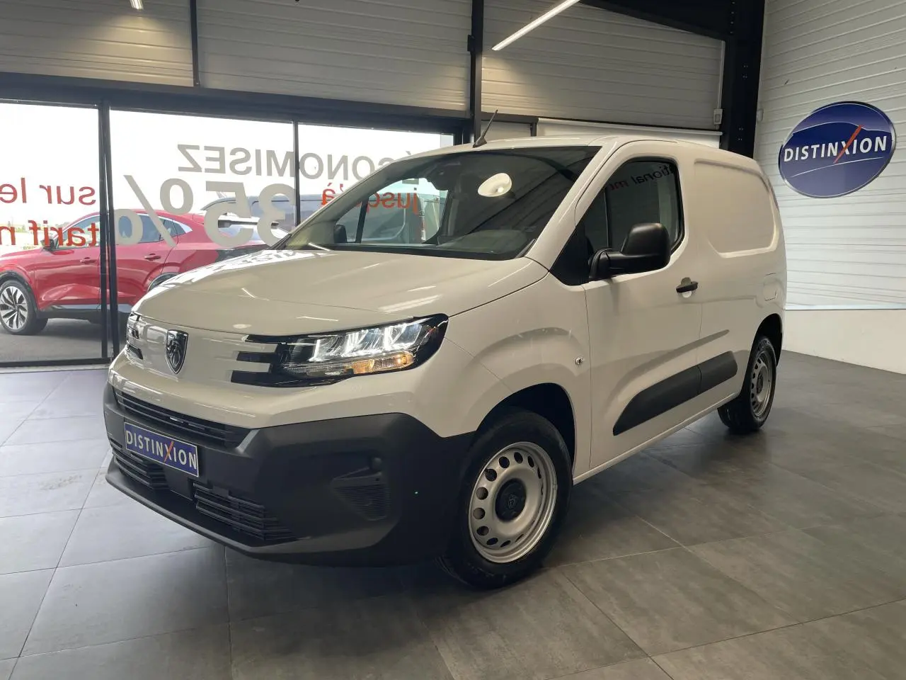 Peugeot Partner blanc en vue 3/4 avant droit, avec pare-chocs noir et jantes tôles grises en showroom.
