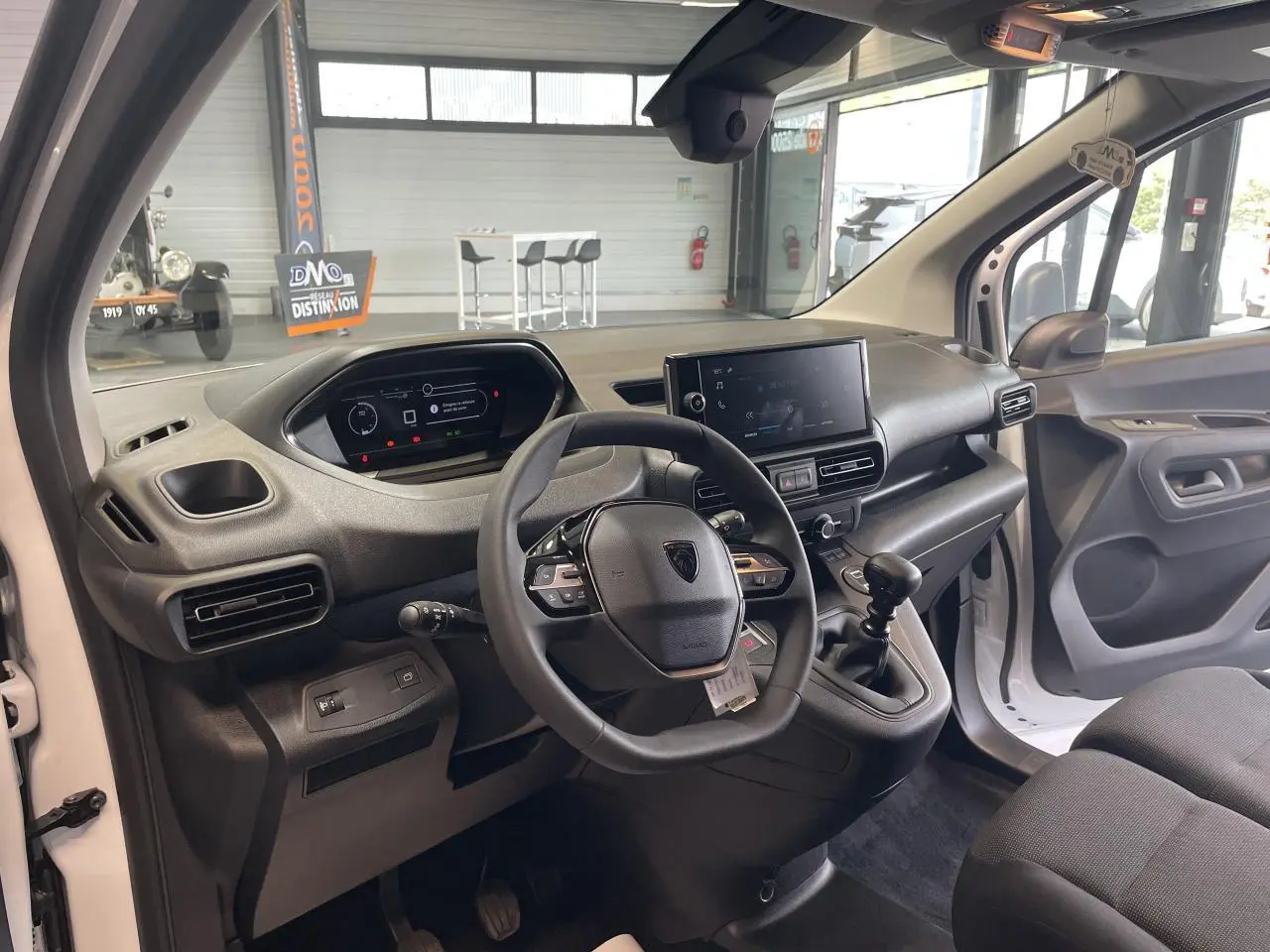 Vue intérieure côté conducteur du Peugeot Partner blanc 2026, montrant le tableau de bord et la console centrale avec boîte manuelle.