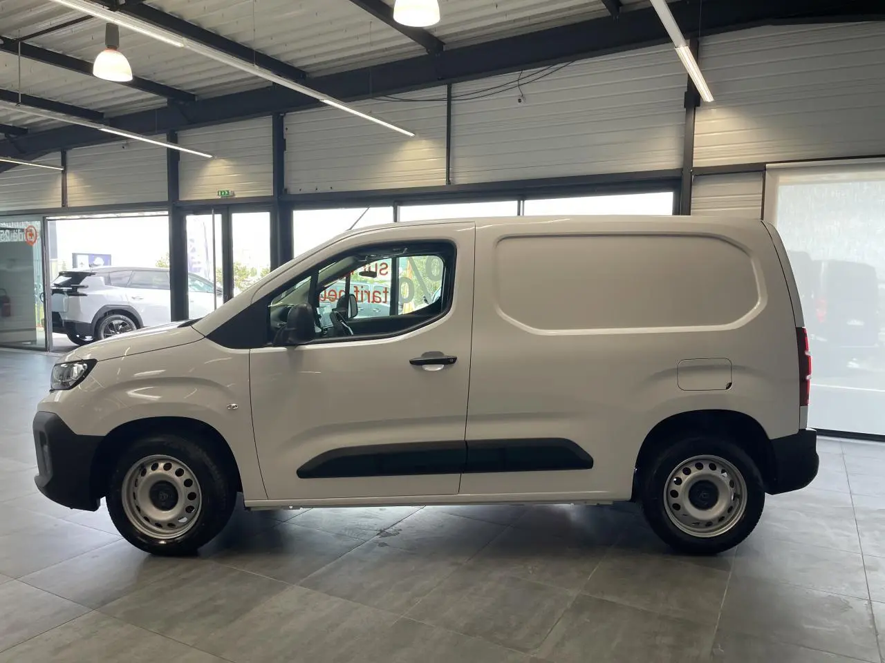 Peugeot Partner blanc en profil droit dans un showroom, avec jantes tôle grises et porte latérale coulissante.