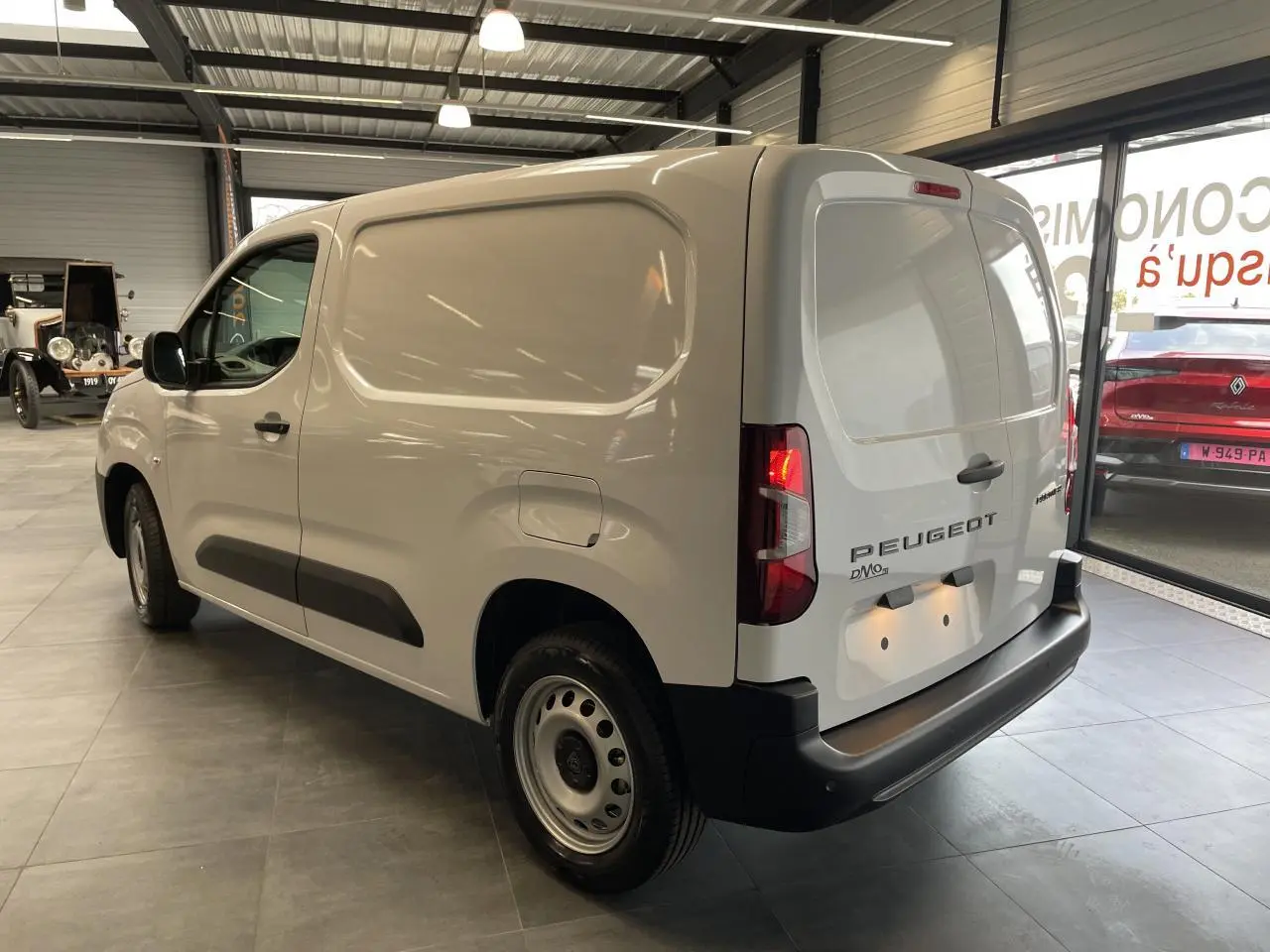 Vue 3/4 arrière droite du Peugeot Partner blanc, fourgon tôlé avec jantes tôle grises en showroom.