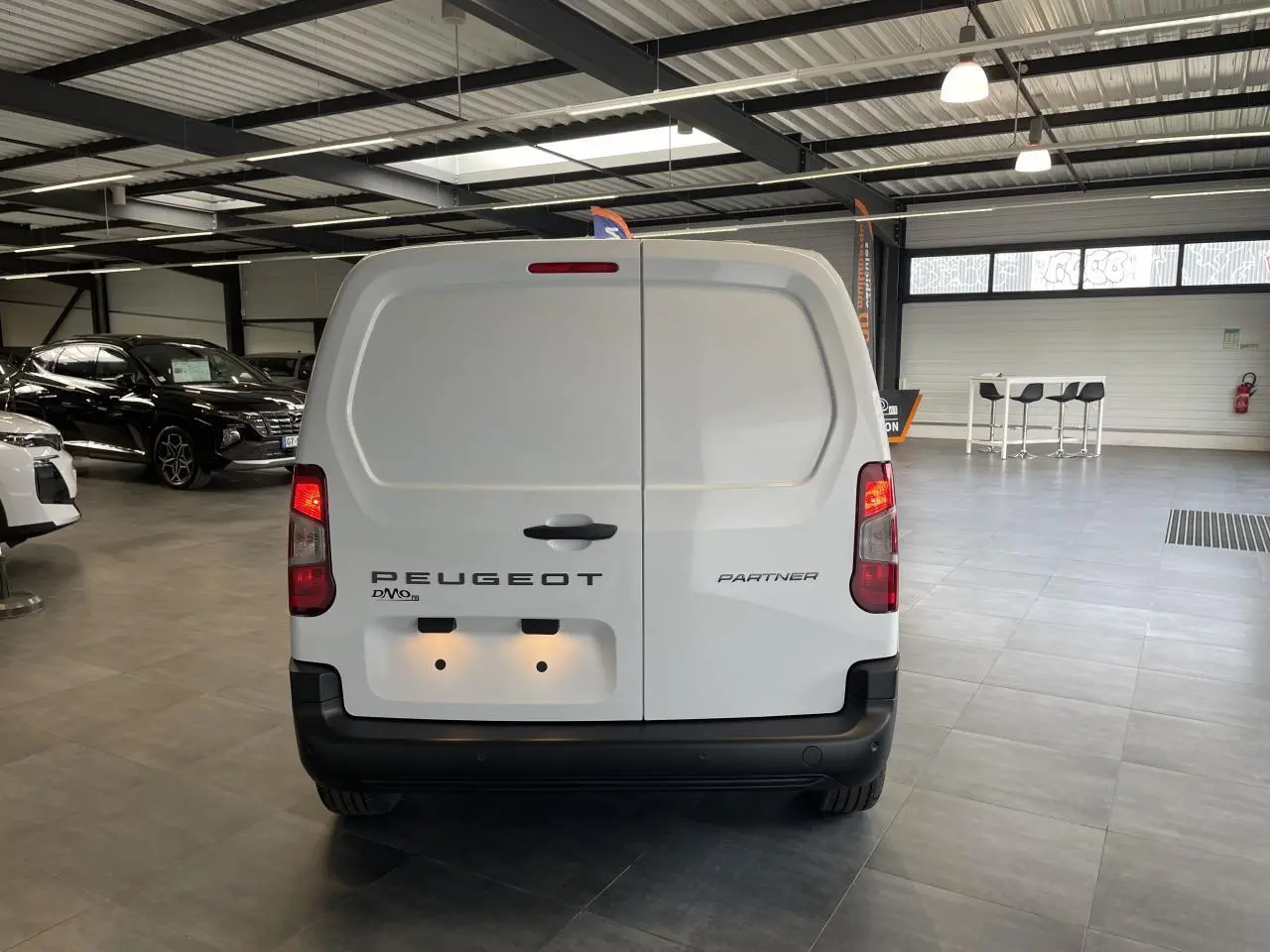 Vue arrière d’un Peugeot Partner blanc stationné en intérieur avec portes battantes fermées et feux allumés.