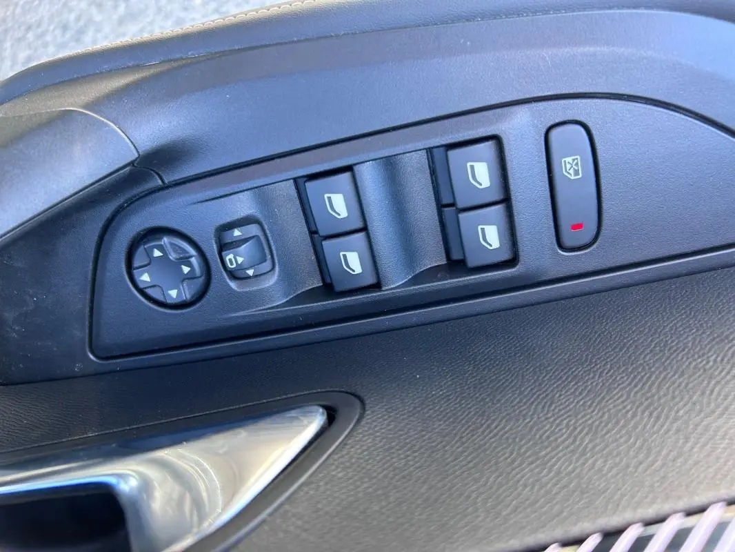 Gros plan sur les commandes électriques des vitres et rétroviseurs côté conducteur du Peugeot 2008 Hybrid noir 2025.