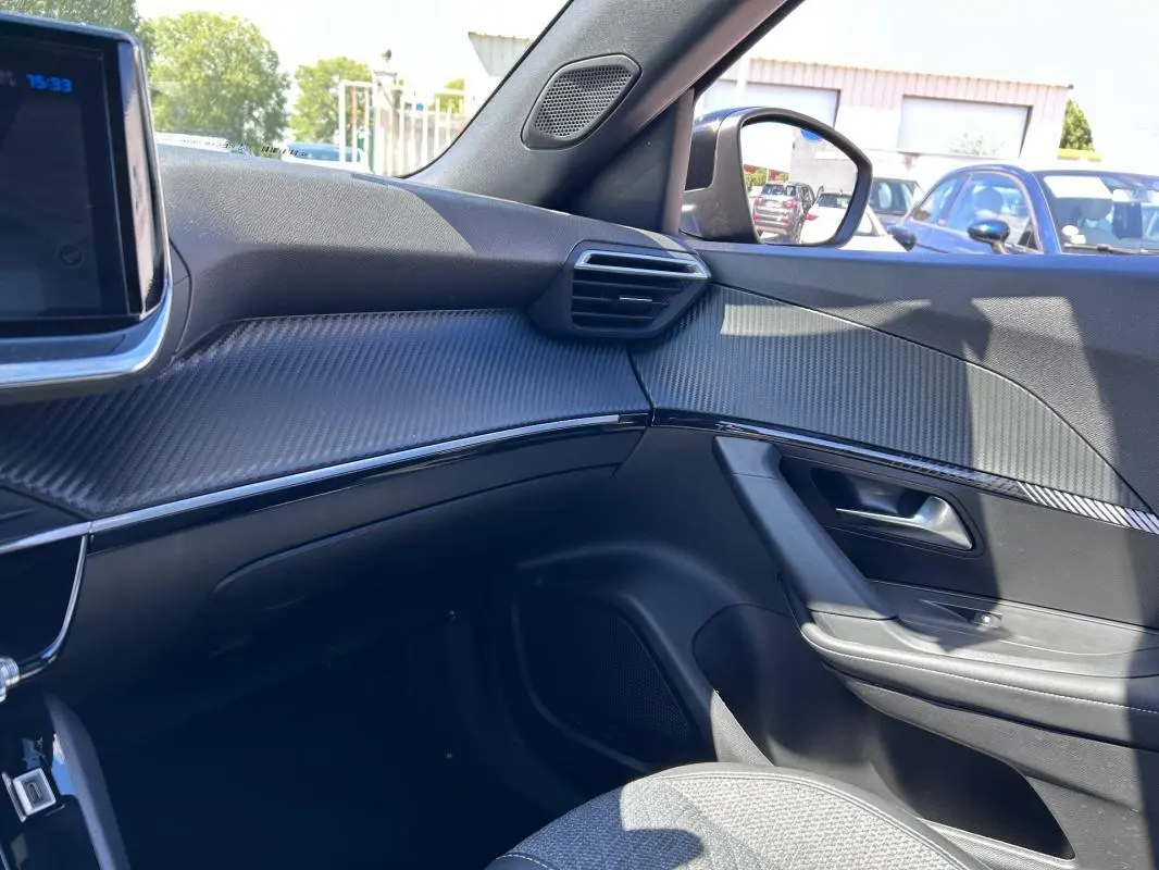Vue intérieure côté passager du Peugeot 2008 Hybrid 136 Allure 2025 noir, avec tableau de bord et garnitures effet carbone.